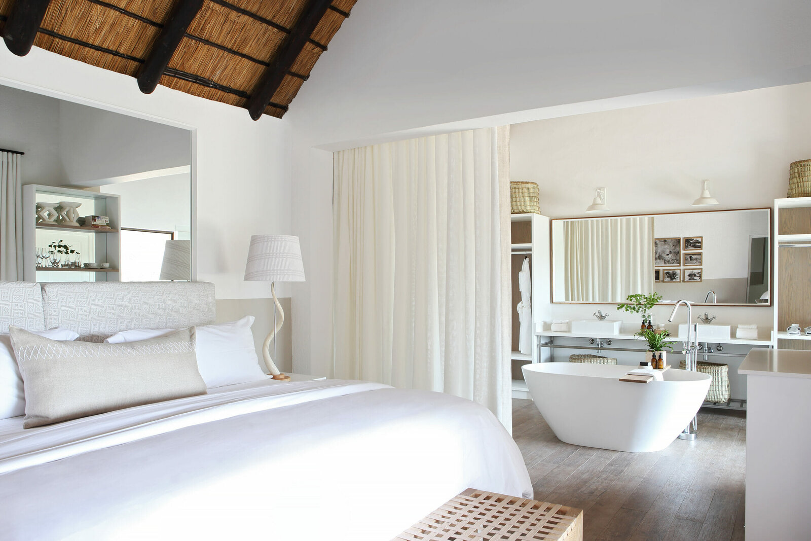 A light-filled suite at Londolozi Varty Camp with a freestanding bath and river views through glass