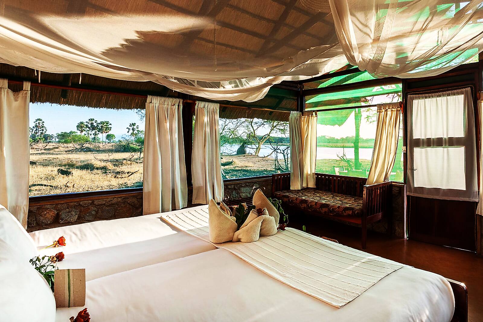 An open, netted four-poster bed in a safari suite framed to the floodplain