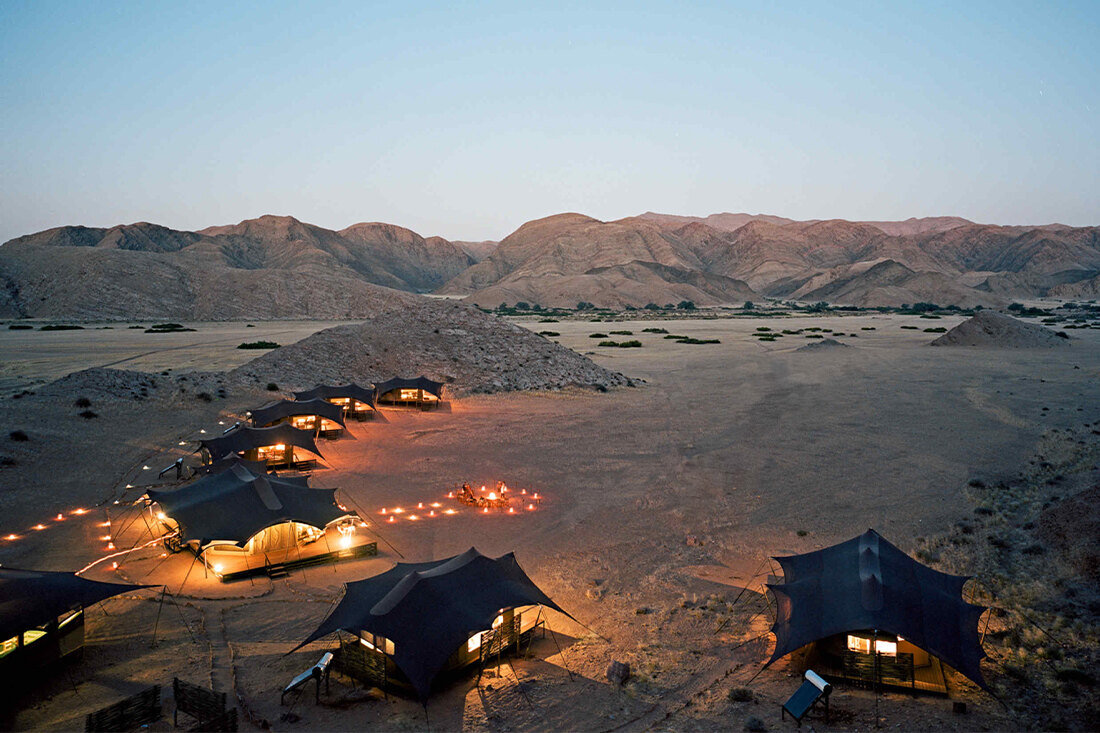 A desert camp glows at dusk among the mountains of Namibia