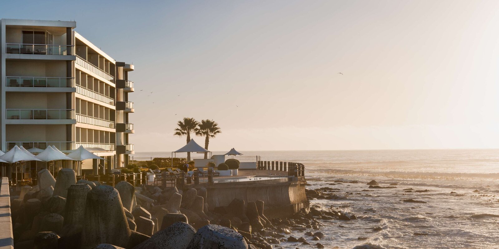 The Radisson Collection Waterfront hotel wing above the rocky Granger Bay coastline at golden hour, the Atlantic beyond