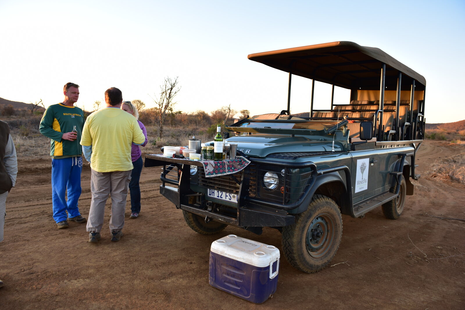 Guests enjoying sundowners beside an open safari vehicle in the bush