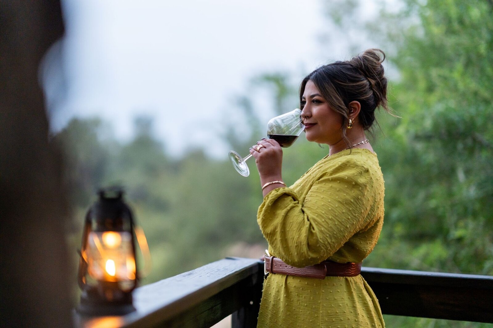 A guest in a yellow dress sipping red wine at dusk beside a lantern on a Silvan Safari deck