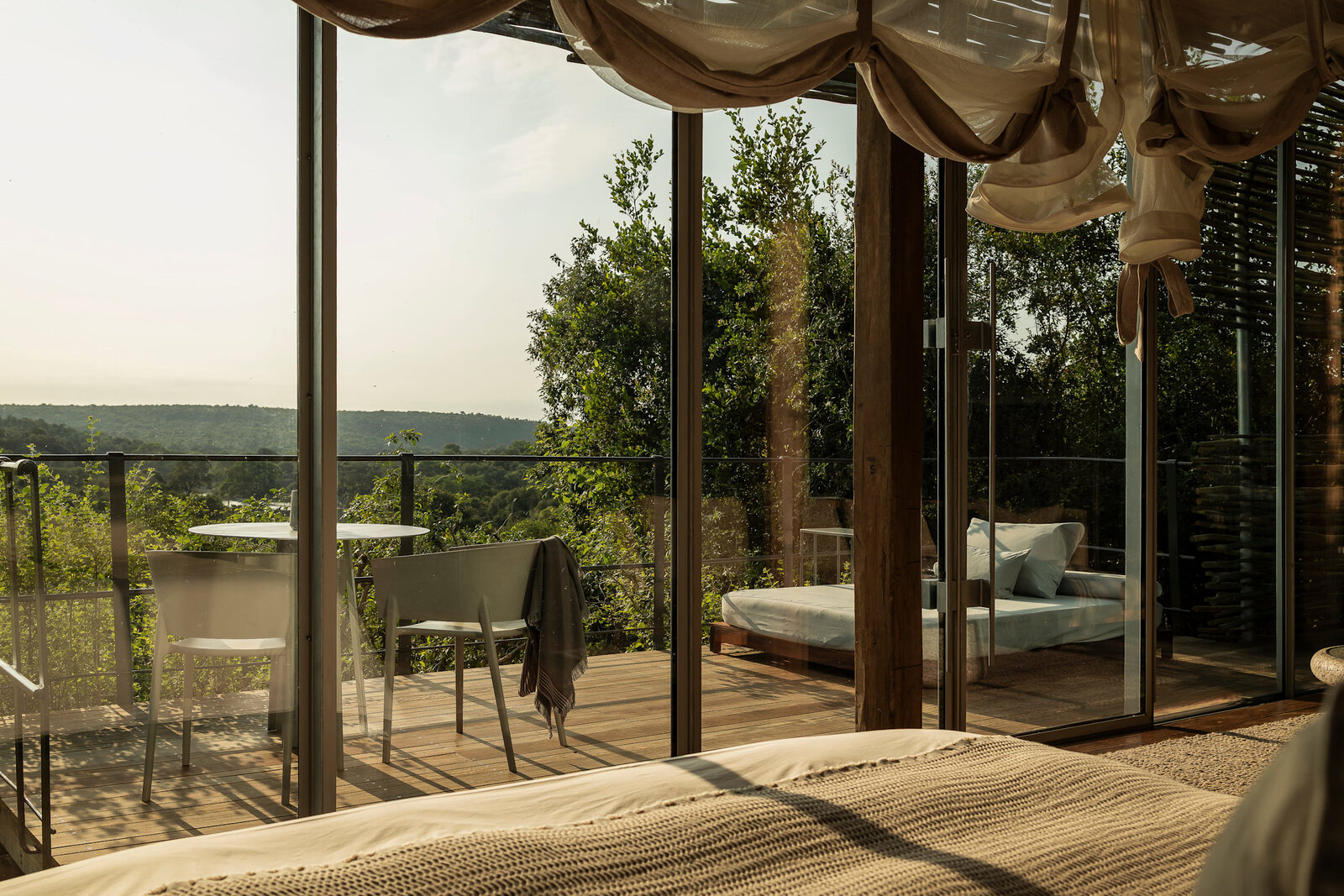 Singita suite bedroom with floor-to-ceiling glass, draped bed and treetop bush views