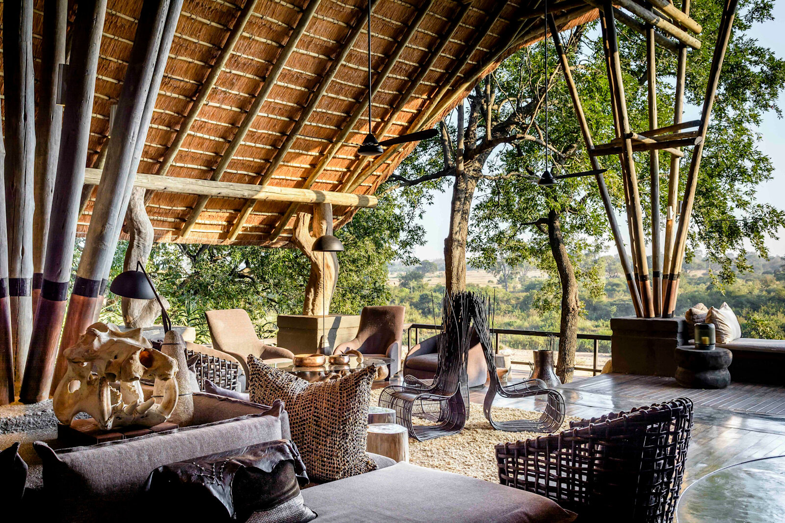 A sheltered open lounge at Singita Boulders Lodge with woven furniture beneath a timber-and-thatch roof
