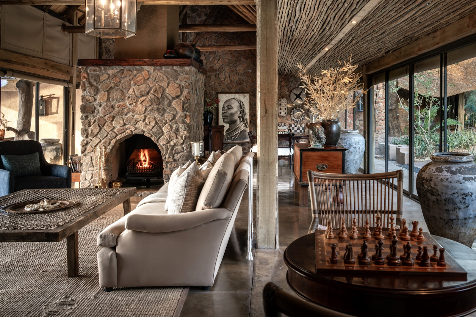 The private lounge of Singita Ebony Villa with a stone fireplace, chess table and glass onto the bush