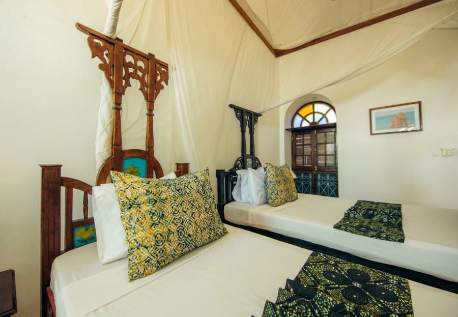 Sultan Suite with a carved Zanzibari four-poster bed and stained-glass windows at The Swahili House, Stone Town