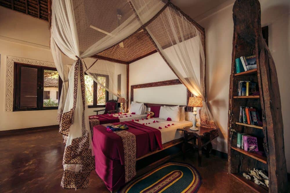 Deluxe Room with a four-poster bed and bookshelves on a polished stone floor at The Swahili House