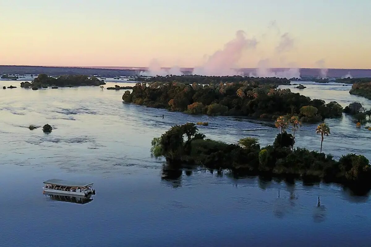 Aerial of the Zambezi River with a boat and Victoria Falls mist beyond