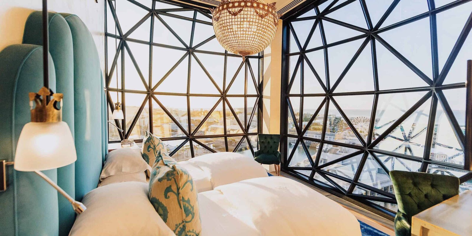 A guest room at The Silo Hotel with bold colour, a chandelier and faceted pillowed-glass windows framing Cape Town