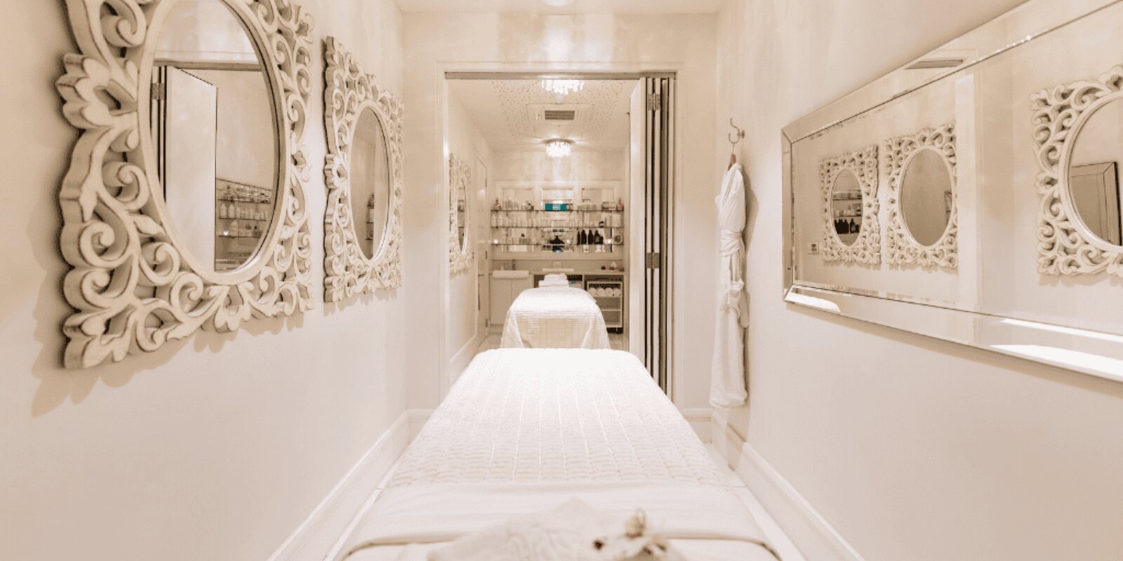 A treatment room corridor at The Silo Spa, white carved mirrors and a chandelier