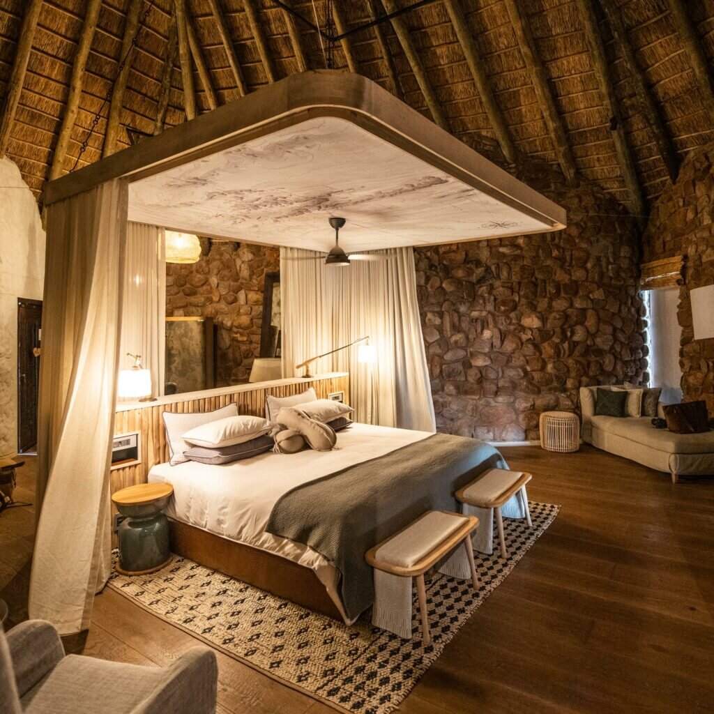 A suite at The Motse with stone walls, thatched roof and warm desert tones