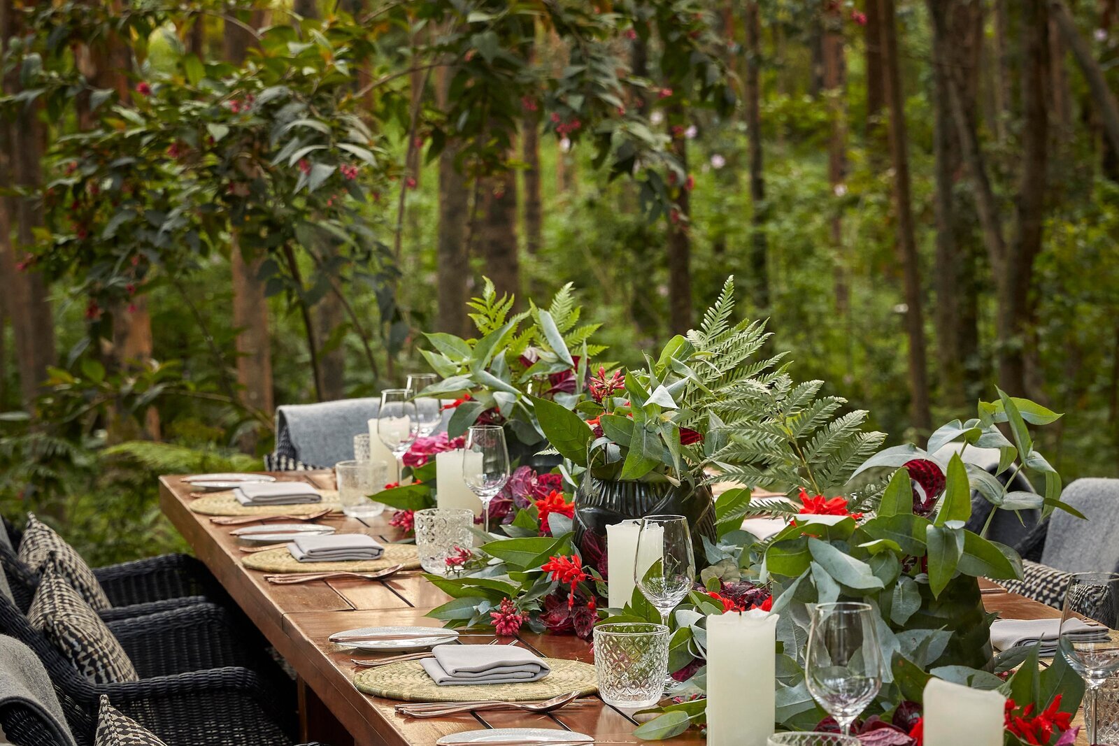 A candlelit table set with flowers and lanterns on a forest lawn in Uganda