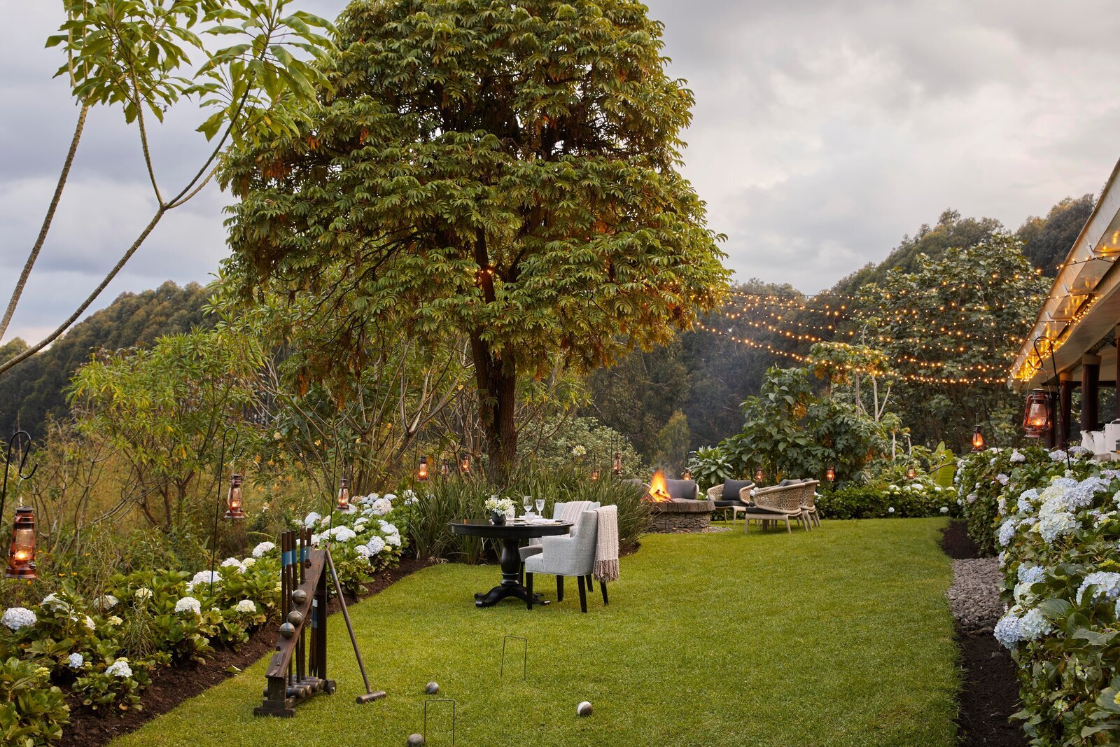 A private table set for two on a forest lawn strung with fairy lights at dusk in Uganda