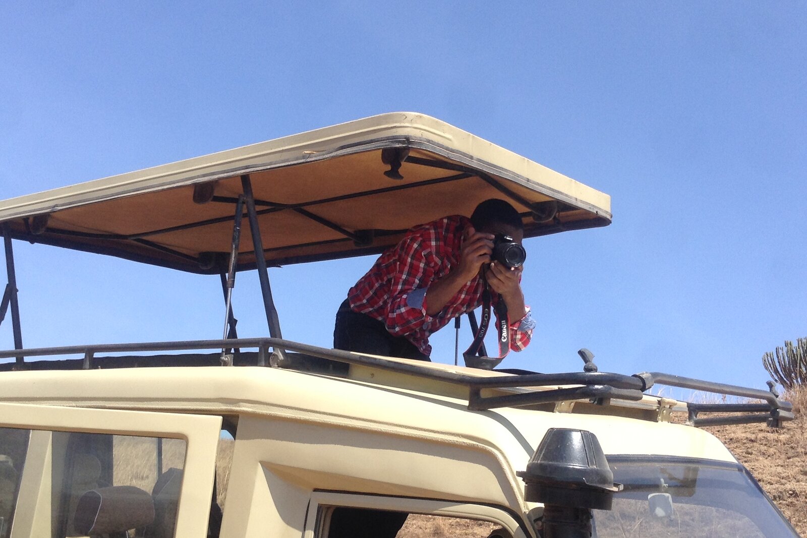 A guest photographing from the roof hatch of a safari vehicle