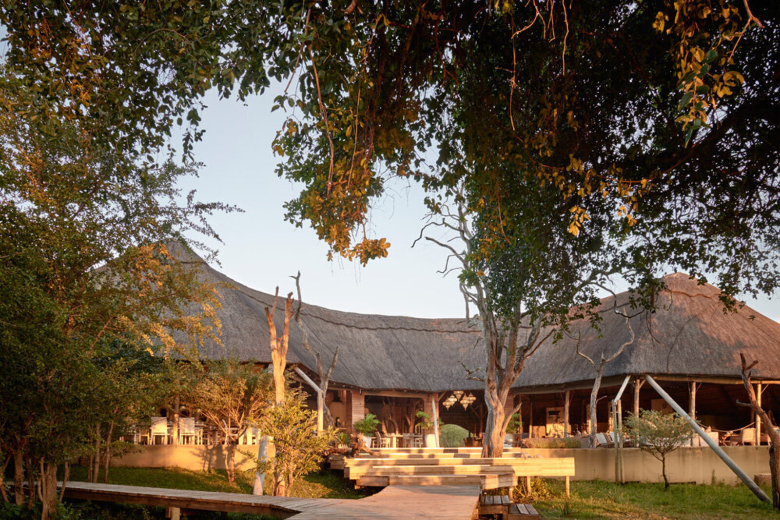 A riverside lodge glowing at dusk under trees on the Zambezi