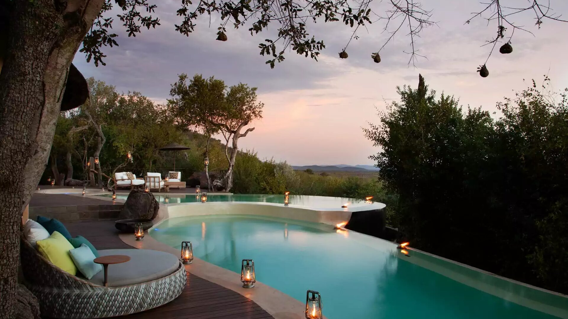 Golden-hour infinity pool at a five-star South African safari lodge lit by lanterns, overlooking the bushveld — 7-day luxury safari packages South Africa 2026