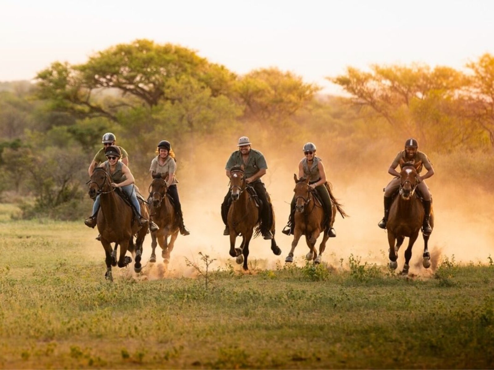 Horse riders cantering through golden African savanna at sunset during a horseback safari