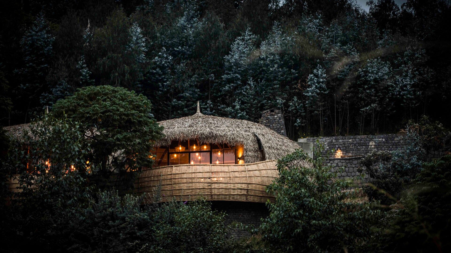 Bisate Lodge's nest-like thatched forest villa glowing at dusk within the eroded volcanic amphitheatre on the edge of Volcanoes National Park, Rwanda