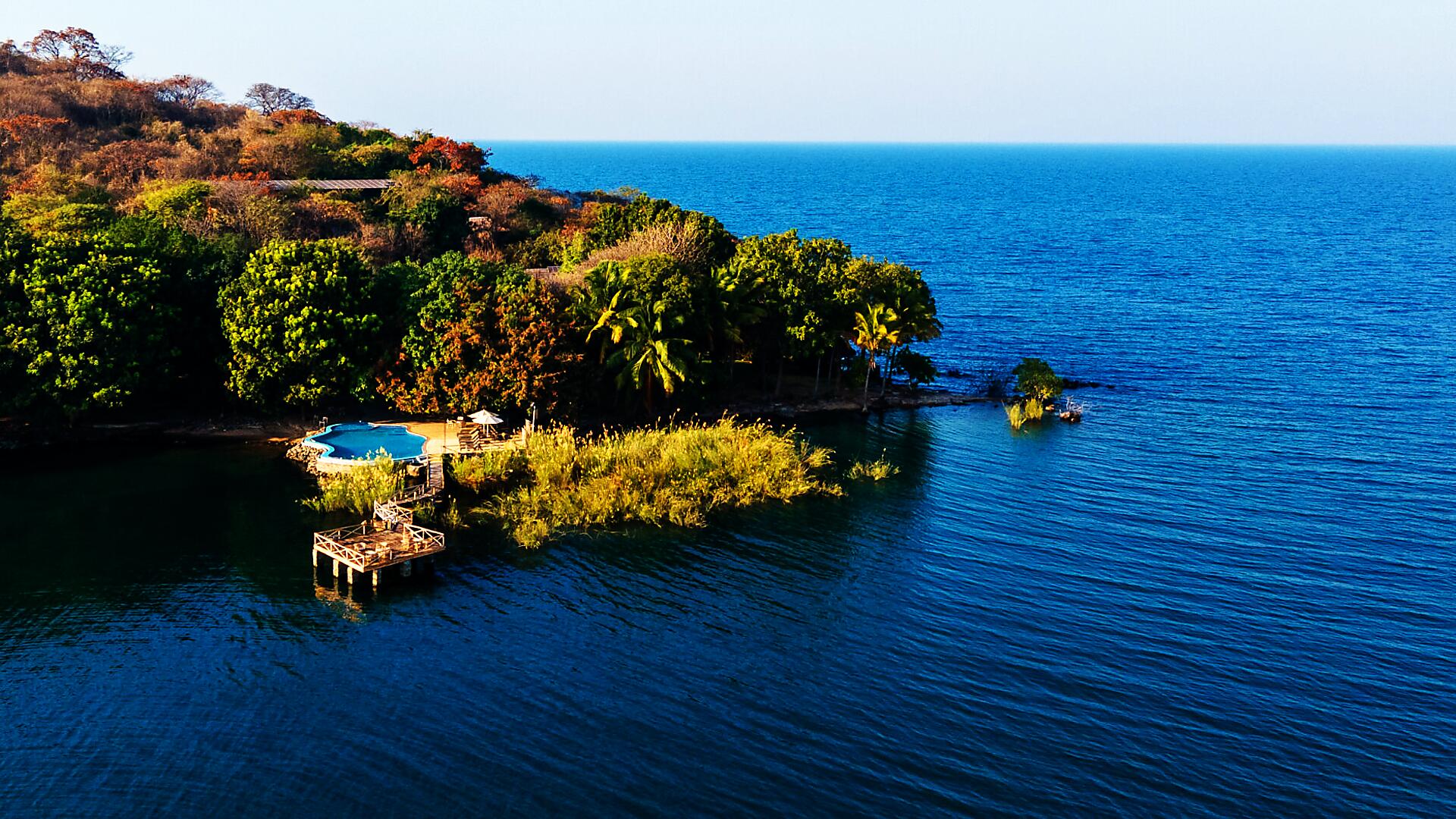 Aerial view of a private forested island lodge set in the blue of Lake Malawi