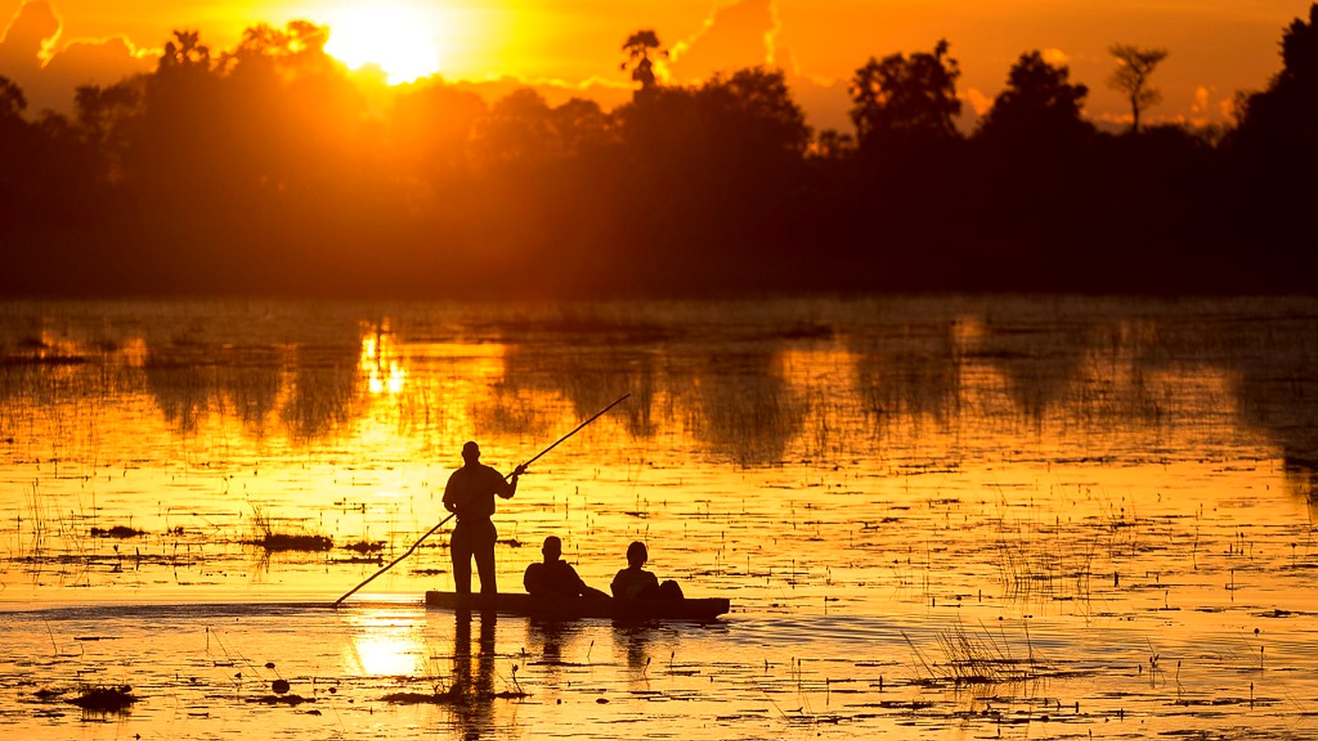 A couple watches the sun set over the Okavango Delta from a private deck with champagne