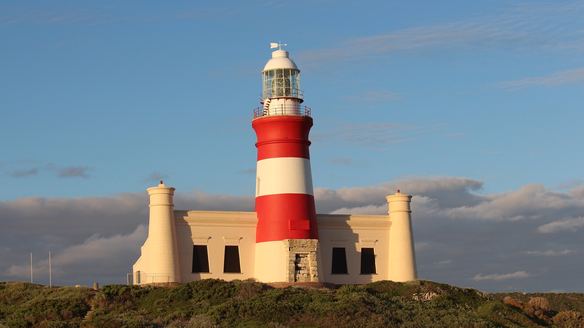 The red-and-white striped Cape Agulhas Lighthouse standing above the fynbos at the southernmost tip of Africa in golden light