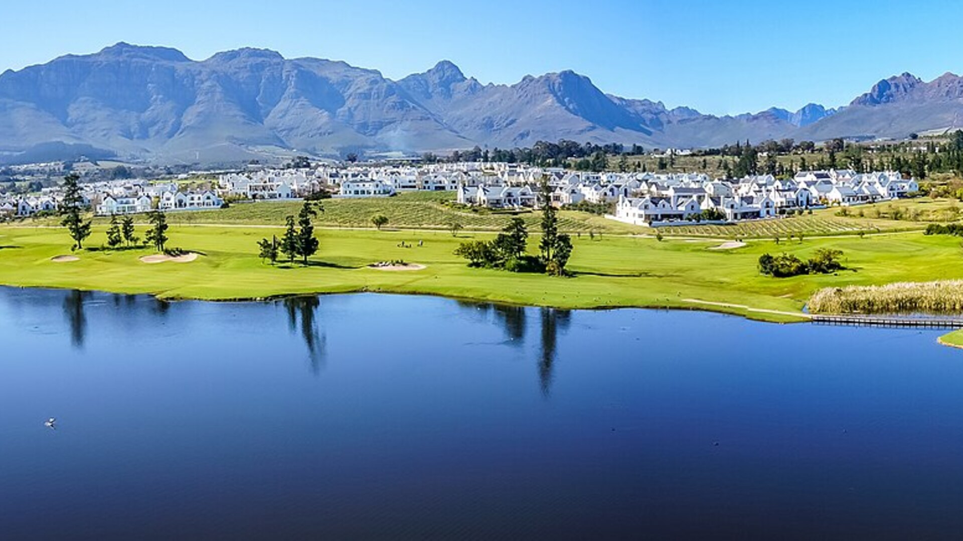 A luxury chauffeured vehicle beside a private wine estate terrace with vineyards and mountains behind at golden hour