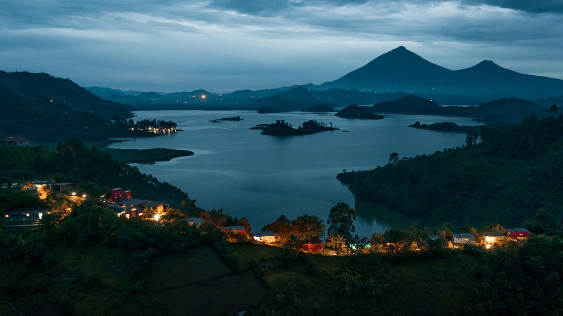 Chameleon Hill Lodge cottages on a ridge above Lake Mutanda with the Virunga volcanoes beyond