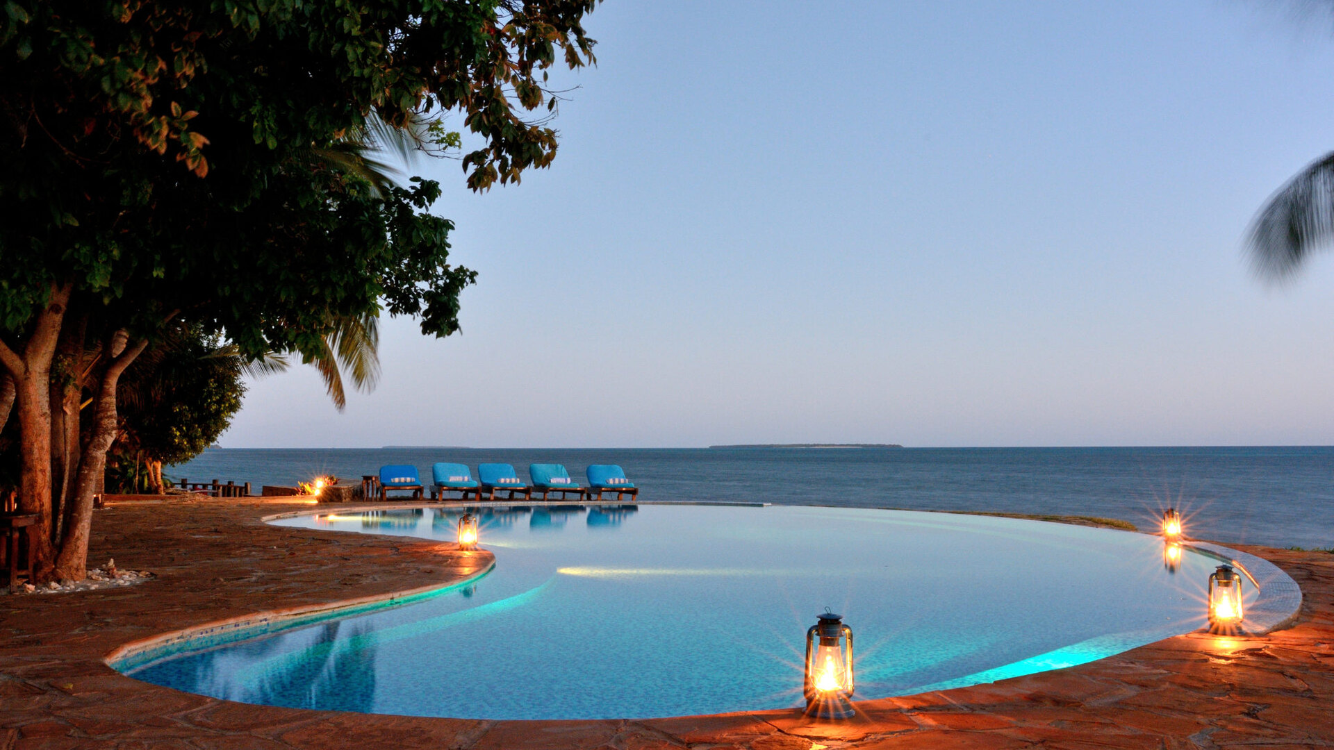 Infinity pool lit by lanterns at dusk at Fumba Beach Lodge, with the Indian Ocean and Menai Bay beyond on the southwest coast of Zanzibar