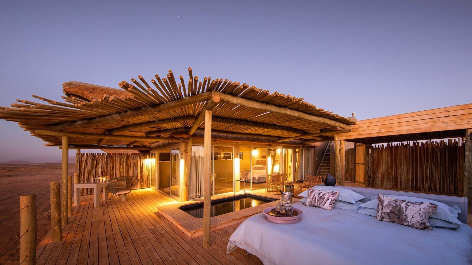 Luxury safari lodge suite with private plunge pool overlooking the red dunes of the Namib Desert at golden hour
