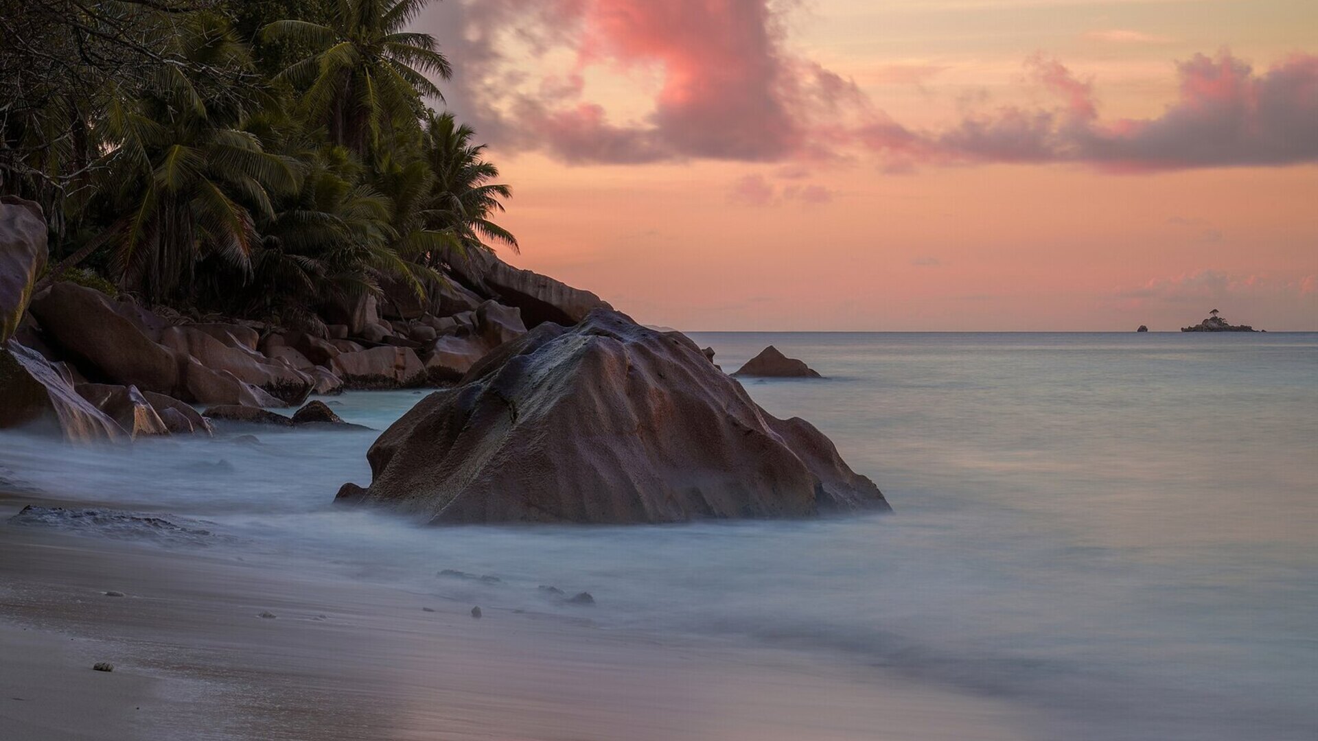 A golden-hour beach in the Seychelles with gentle surf and thatched umbrellas