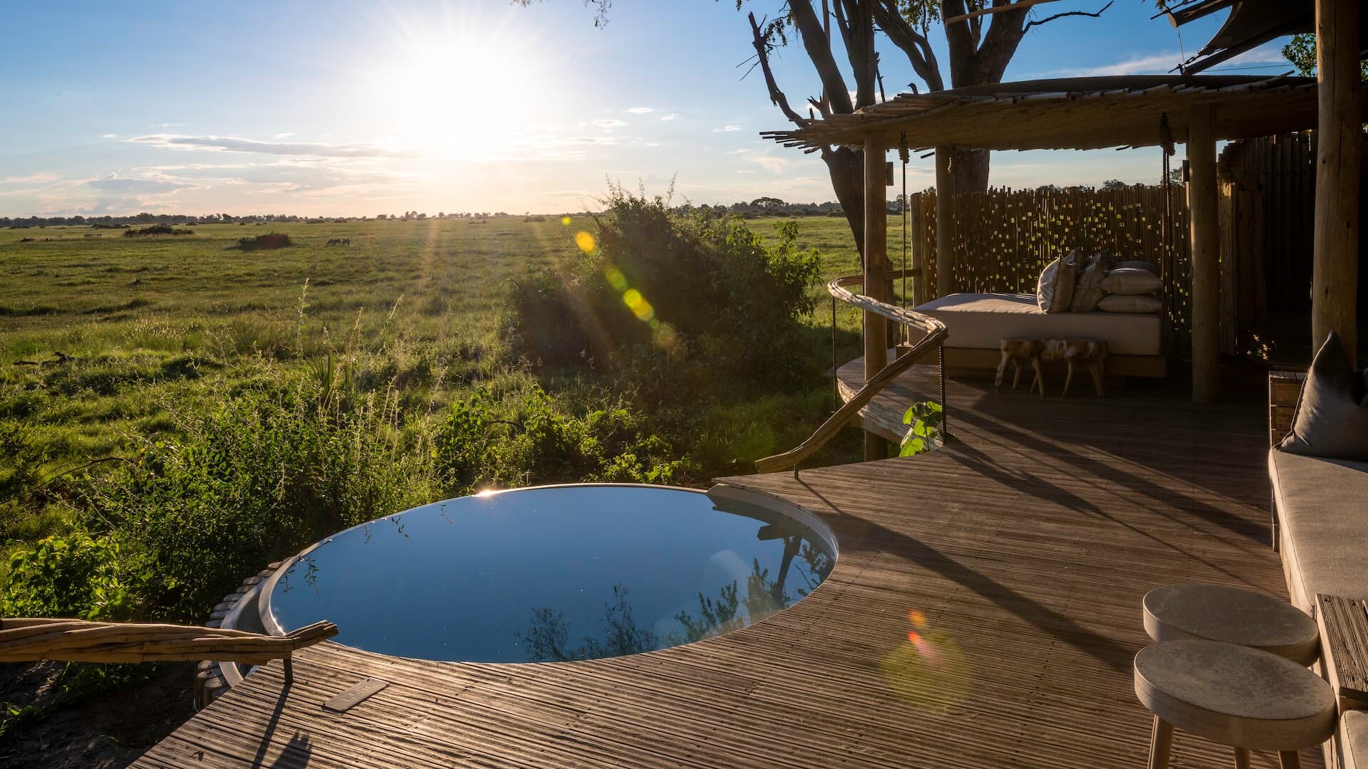 A private plunge pool on an elevated timber suite deck at Mombo Camp, catching golden light over the Okavango floodplain