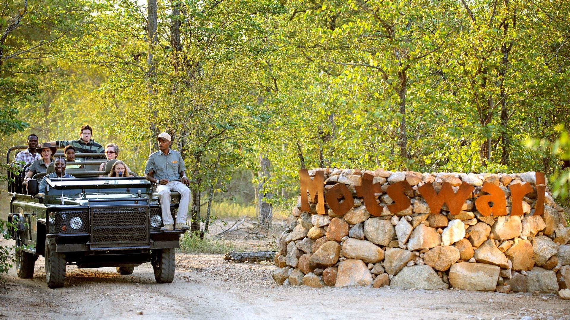 Guests head out on a game drive in an open Land Rover past the Motswari Private Game Reserve stone entrance sign in the Timbavati