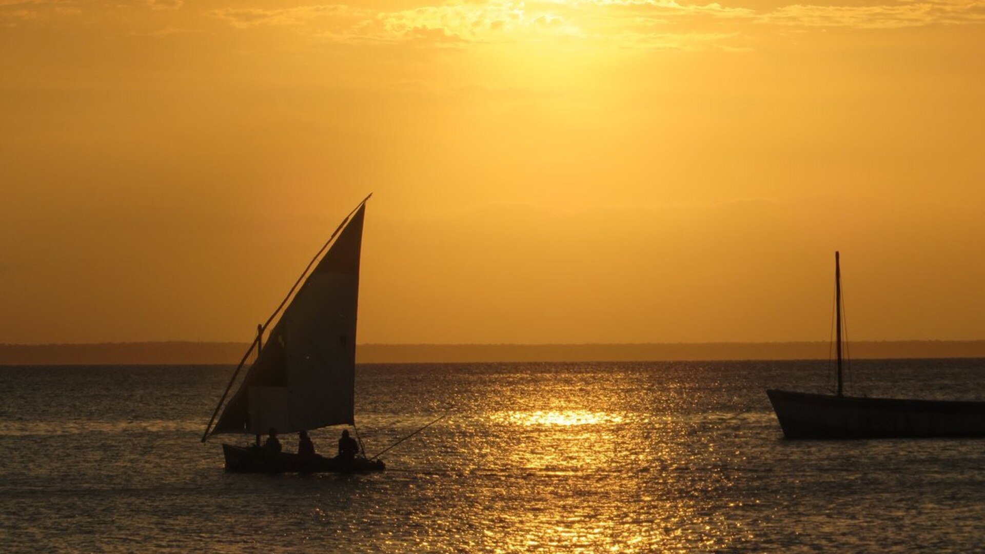 A traditional dhow sailing into a golden Indian Ocean sunset, comparing Mozambique and Zanzibar honeymoon islands