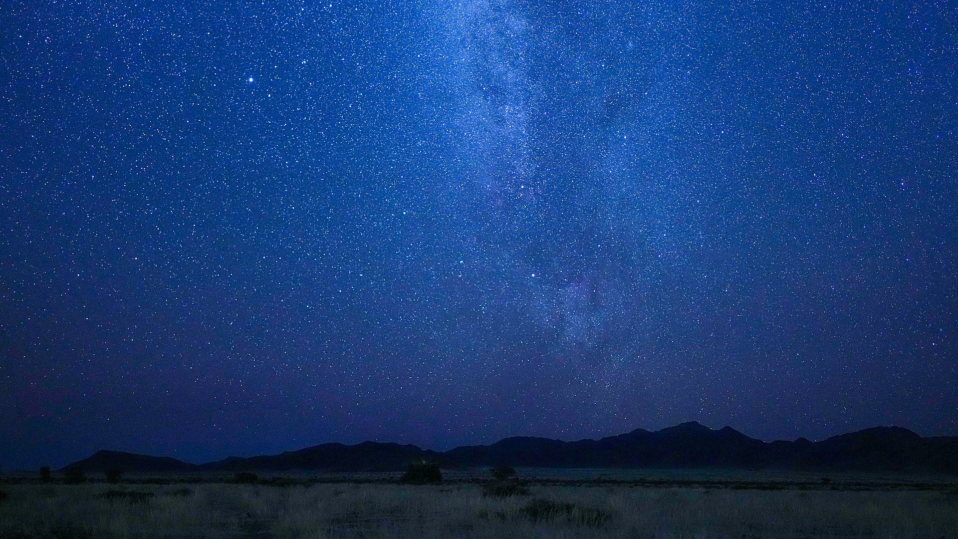 The Milky Way galaxy stretching across the night sky above the desert mountains of the NamibRand Nature Reserve