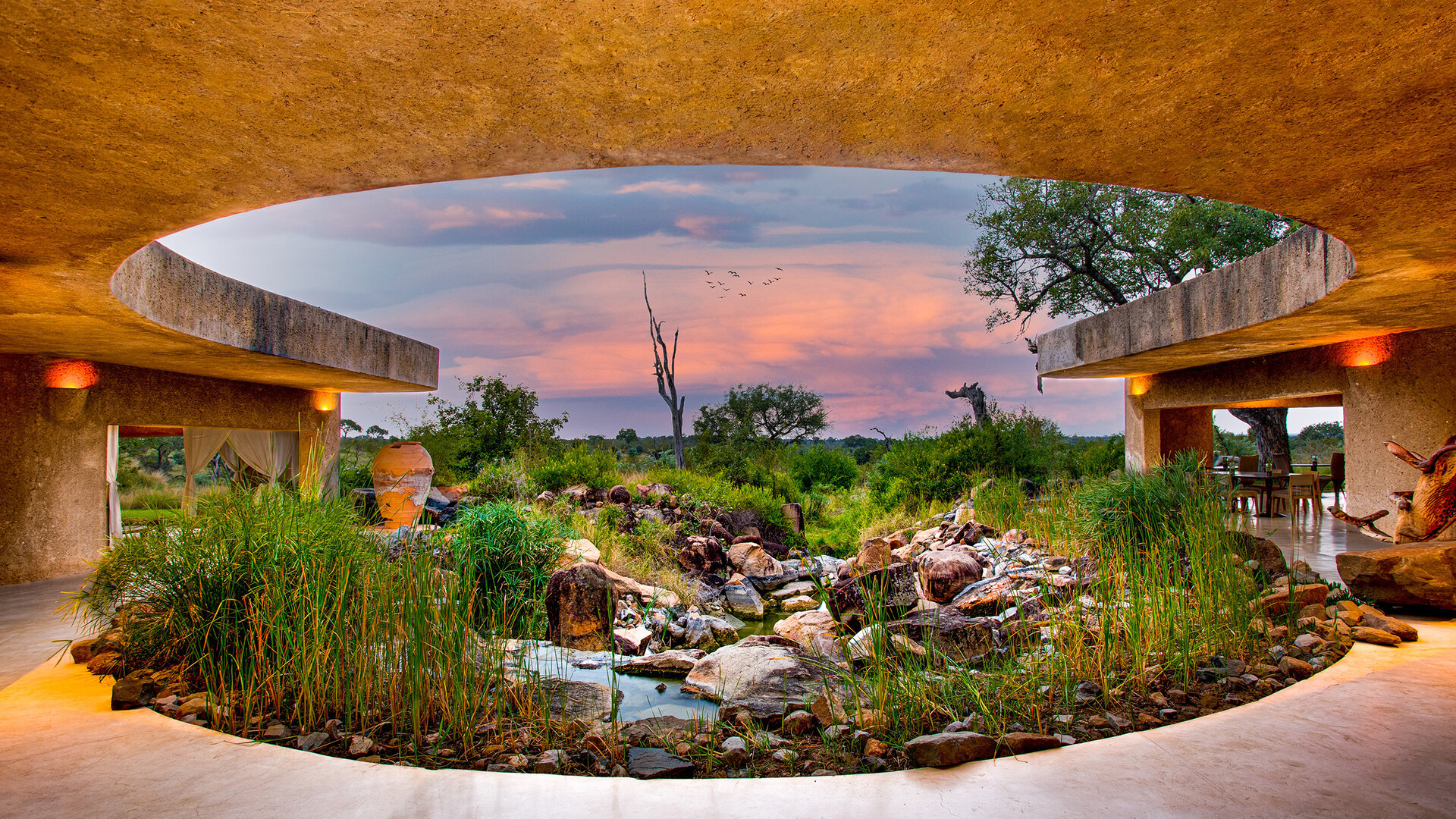 Sabi Sabi Earth Lodge's iconic circular courtyard entrance with water feature at golden hour in the Sabi Sand Game Reserve