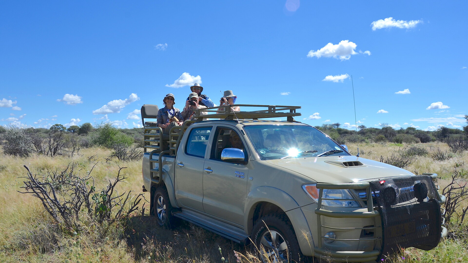 Guests standing in an open safari vehicle under a bright Kruger sky