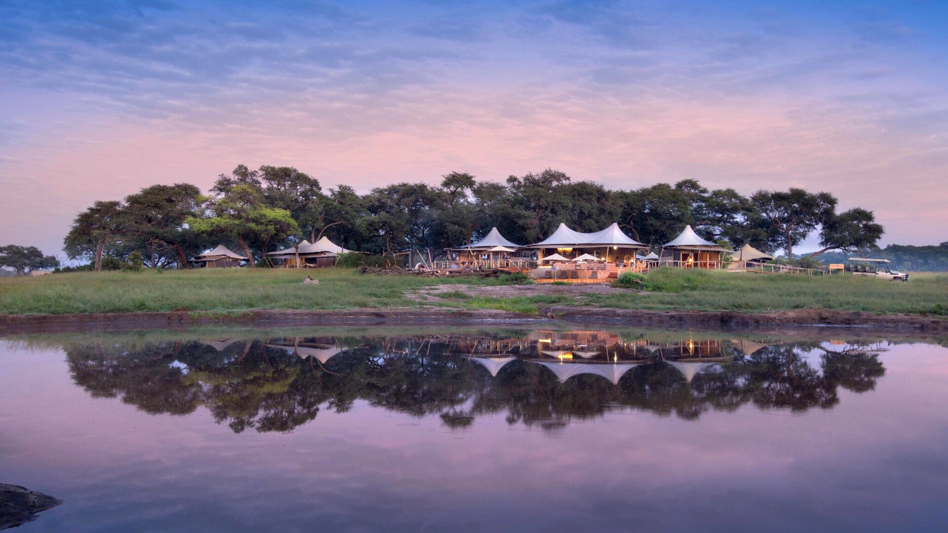 Somalisa Camp tents reflected in a still Hwange pan at dusk, Zimbabwe