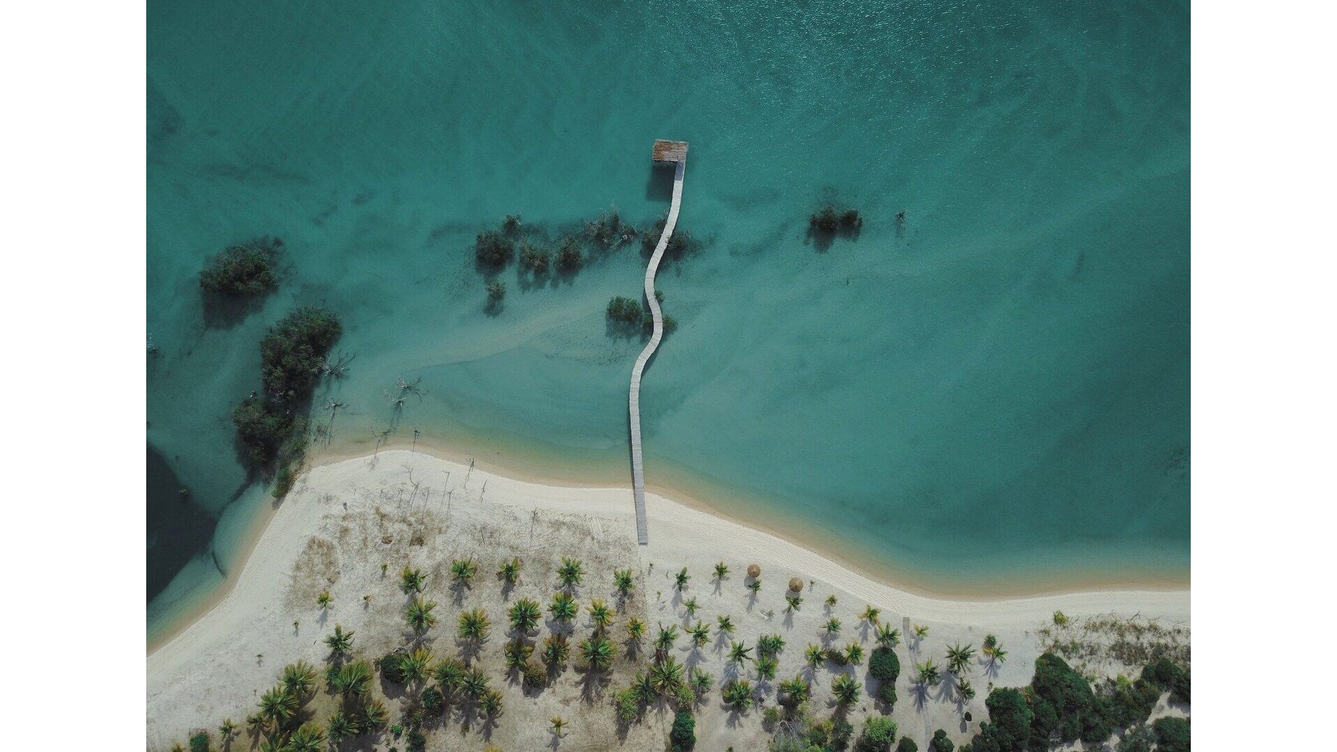 Aerial view of Sussurro Beach Lodge on the remote Nhamabue Peninsula, showing six minimalist bungalows scattered along pristine white beach, Mozambique