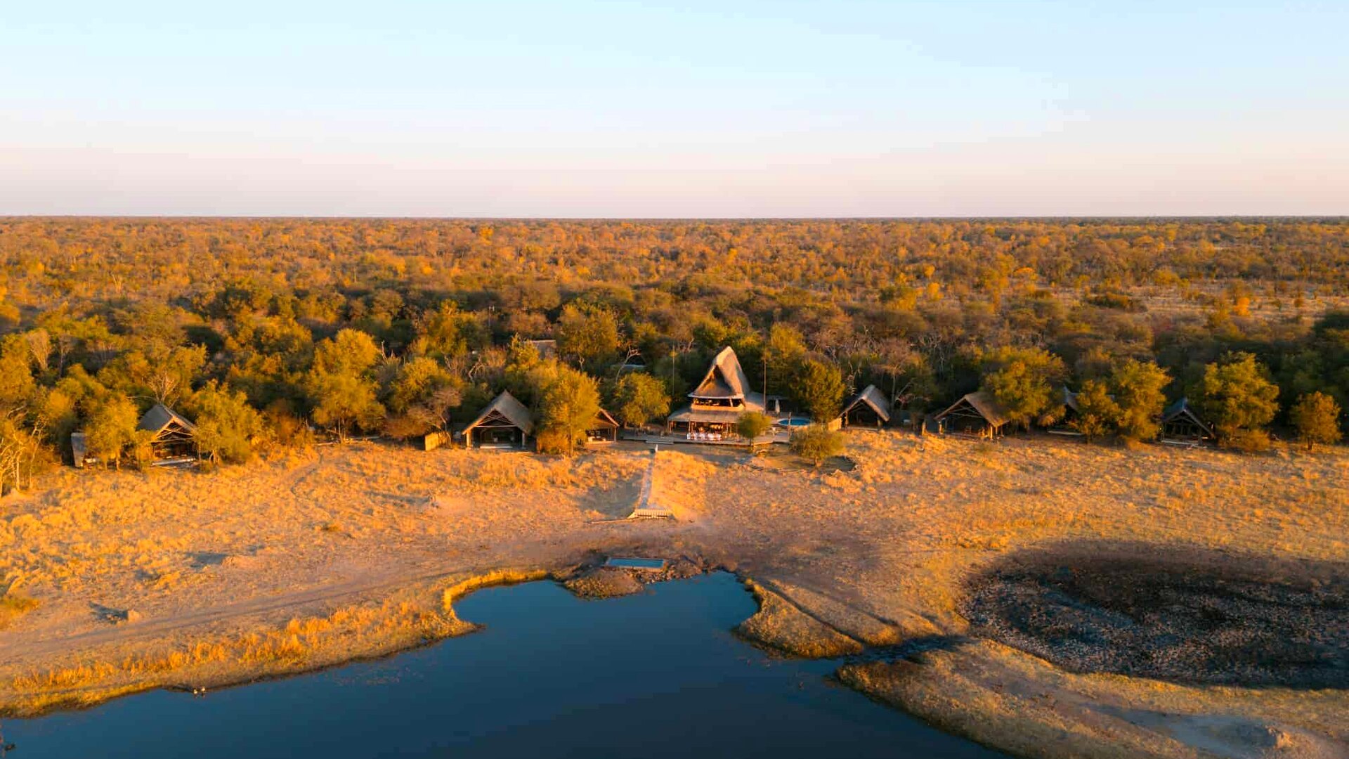 Aerial view of The Hide camp beside a floodlit Hwange waterhole at golden hour