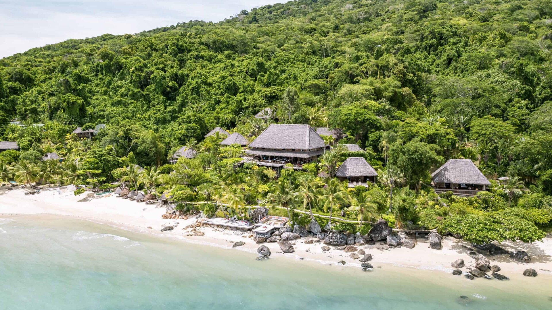 Aerial view of Time + Tide Tsara Komba's villas nestled in the lush forest slopes above a turquoise bay on Nosy Komba island, Madagascar