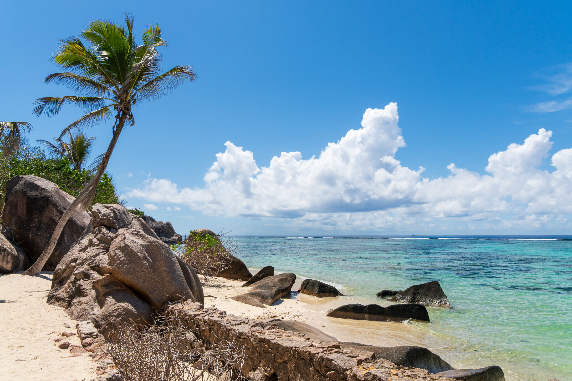 Weather-worn granite boulders on a white-sand beach at La Digue, Seychelles, a calm turquoise bay beyond — Top 10 Best Seychelles holiday packages 2026 and 2027