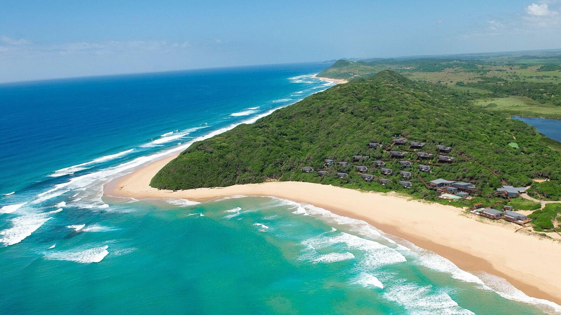 Aerial view of an untouched golden Mozambique beach and turquoise Indian Ocean, with a luxury lodge tucked into the dune forest at Ponta Mamoli