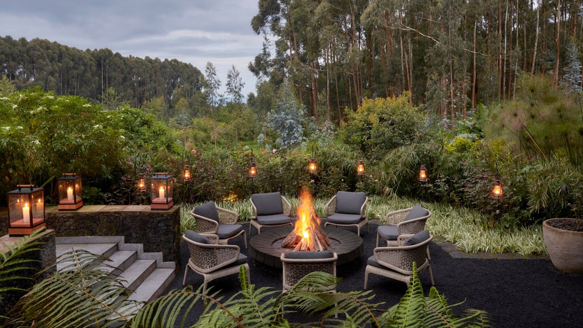 A lantern-lit firepit boma glowing at dusk at a luxury forest lodge in Uganda