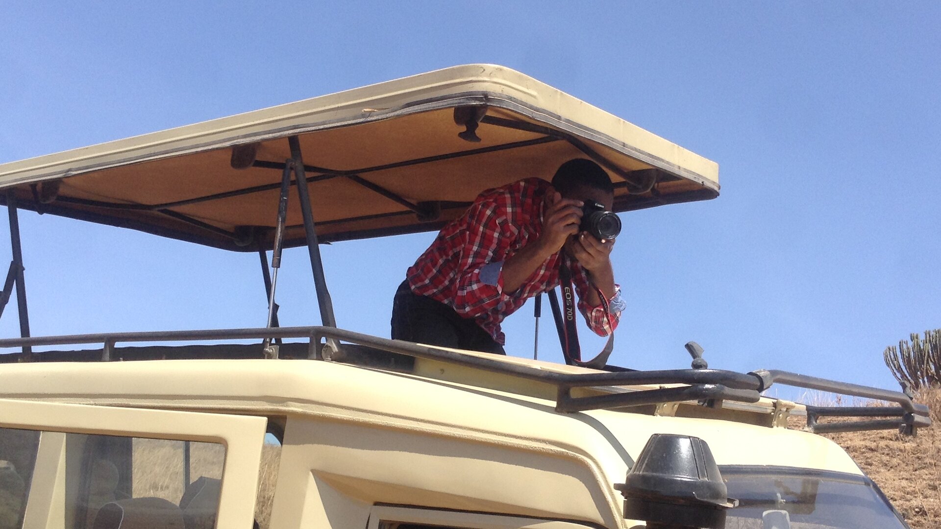 A guest photographing from the raised roof hatch of an open safari vehicle in Kruger