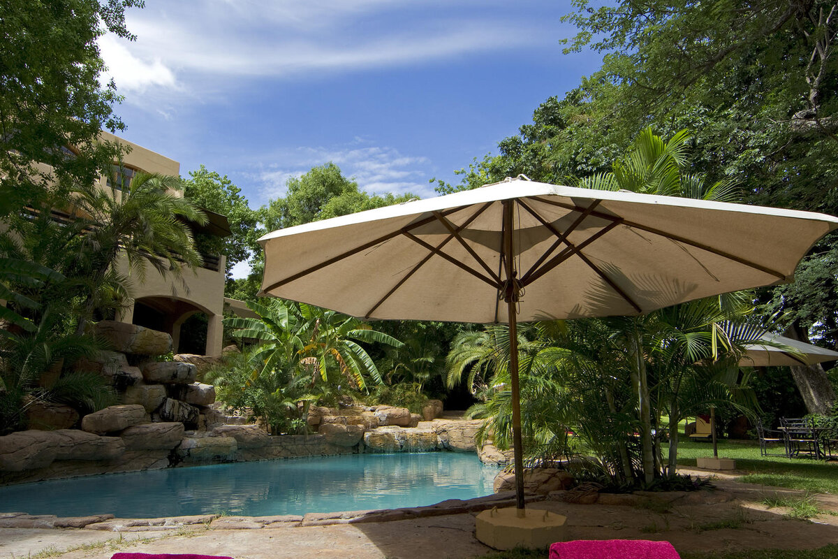 Lush garden and pool with parasol at Chobe Game Lodge inside Chobe National Park