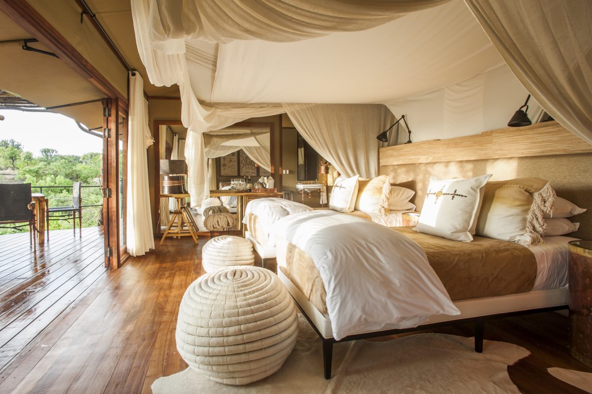 A Mwiba tented suite — king bed on a raised deck, built into the granite outcrop above the gorge.