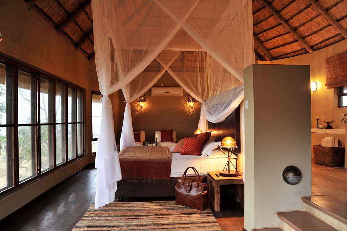 Ngoma Safari Lodge luxury suite interior with four-poster bed, floor-to-ceiling windows and Chobe views