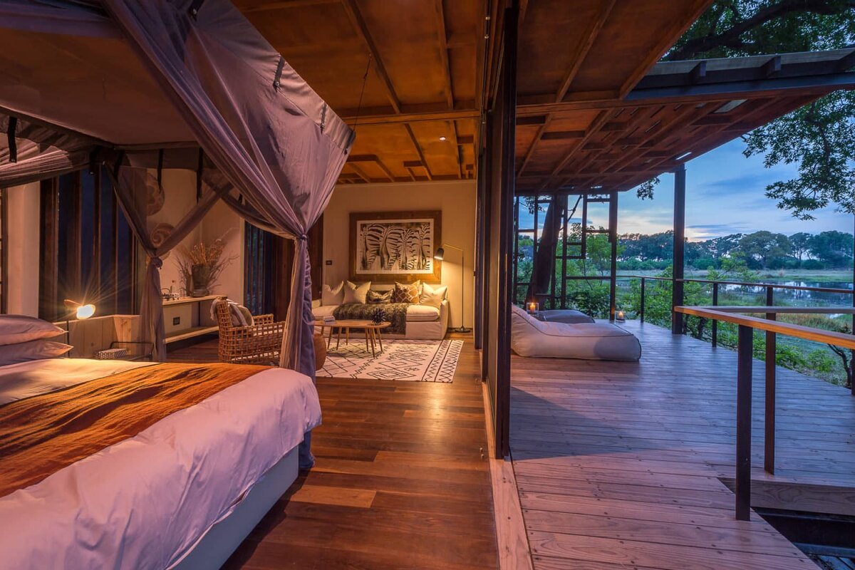 Qorokwe Camp luxury suite opening onto a private timber deck overlooking an Okavango Delta lagoon at dusk