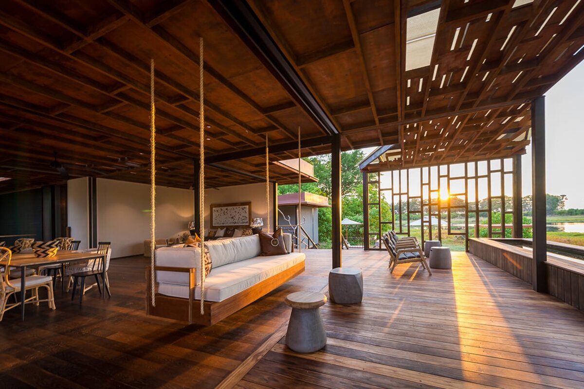 Qorokwe Camp contemporary lounge with hanging daybed and floor-to-ceiling glass framing the Okavango sunset