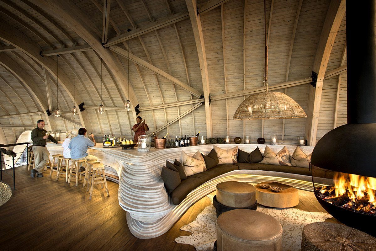 andBeyond Sandibe curved timber lounge and bar with fireplace, Okavango Delta Botswana all-inclusive lodge